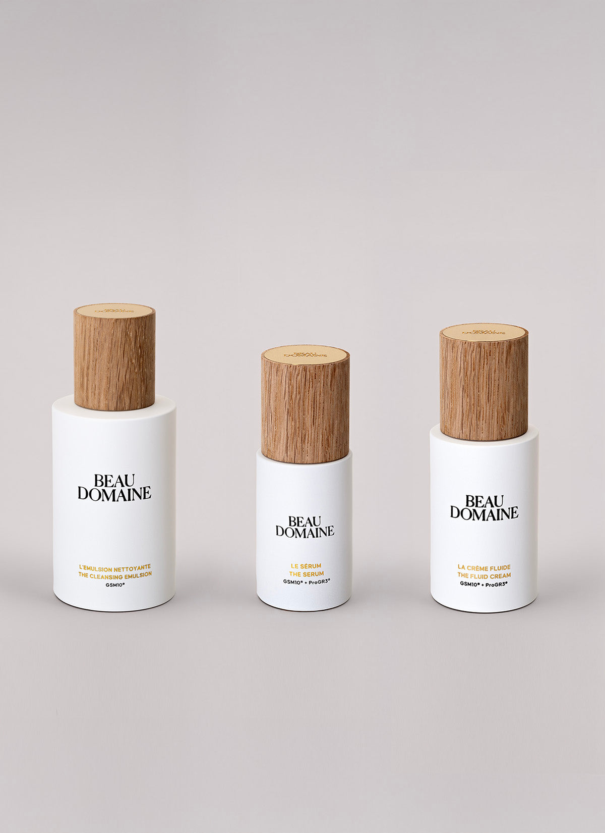 Three 'Beau Domaine' skincare bottles with wooden caps on a light gray background